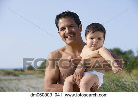 Stock Image - Hispanic father holding baby at beach. Fotosearch