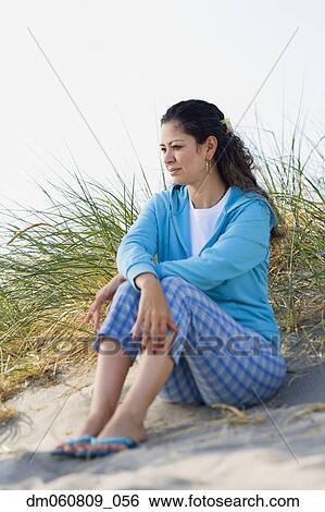 Stock Photograph - Hispanic woman sitting in sand at beach. Fotosearch