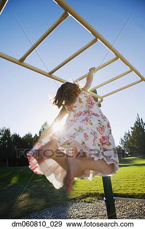 Stock Photo - Low angle view of girl hanging on play structure. Fotosearch