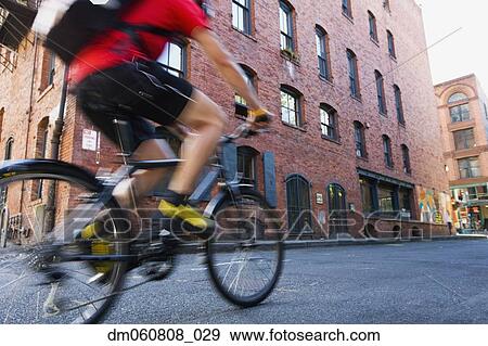 Low angle view of man riding bicycle on street View Large Photo Image Stock Photo - Low angle view of man riding bicycle on street. Fotosearch