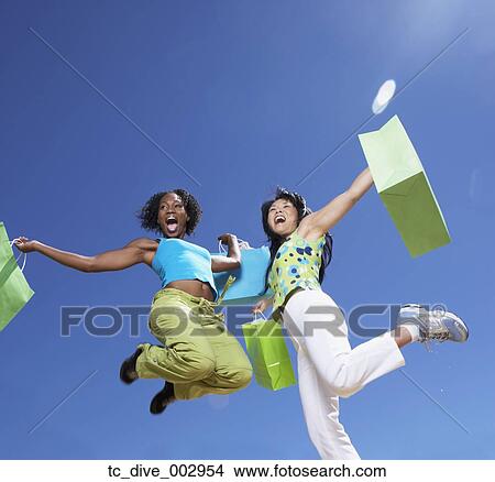 Picture - Low angle view of two women jumping with shopping bags. Fotosearch