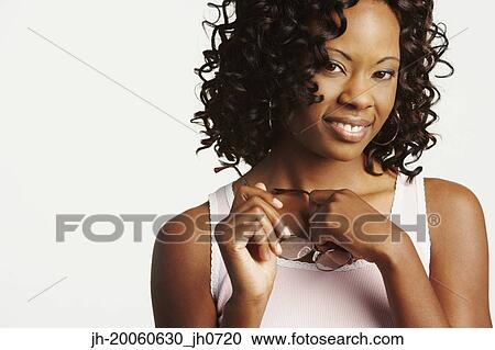 Stock Image - Studio shot of African woman holding eyeglasses and smiling. Fotosearch