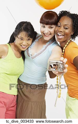 Stock Image - Studio shot of three women taking own photograph . Fotosearch