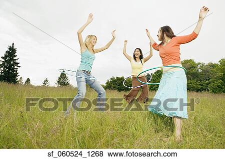 Three young women playing with hula hoops in meadow View Large Photo Image Stock Photo - Three young women playing with hula hoops in meadow. Fotosearch