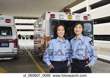 Stock Image - Two Asian female paramedics smiling in front of ambulance. Fotosearch