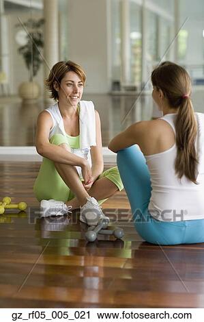 Stock Image - Two women sitting on floor with dumbbells. Fotosearch