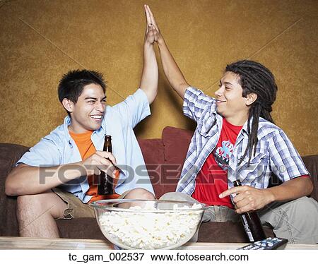 Stock Photo - Two young men high-fiving on sofa . Fotosearch