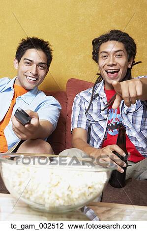 Stock Image - Two young men on sofa with popcorn and remote control. Fotosearch