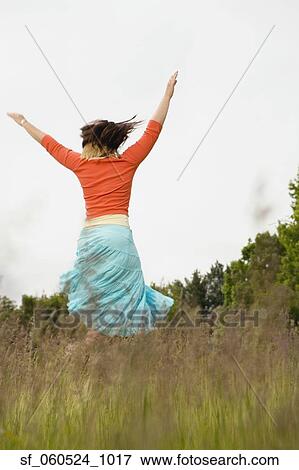 Stock Photo - Woman dancing with arms raised in meadow. Fotosearch