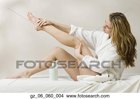 Picture - Woman in bathrobe applying lotion to leg. Fotosearch
