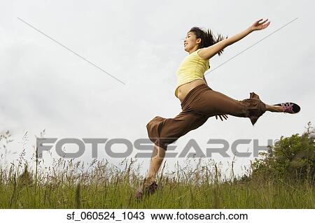 Stock Image - Woman jumping with arms out in meadow. Fotosearch