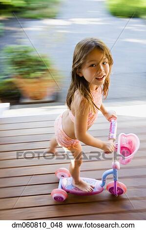 Stock Photo - Young Asian girl riding foot powered scooter outdoors. Fotosearch