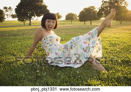 Stock Image - Young Asian woman kicking up foot in grass outdoors. Fotosearch