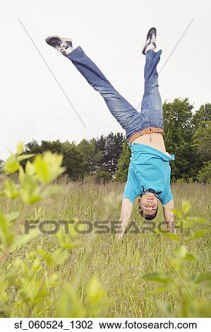 Stock Image - Young man performing handstand in meadow. Fotosearch