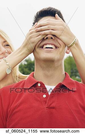Stock Photography - Young woman covering young man's eyes outdoors. Fotosearch