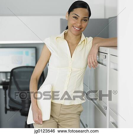 Stock Photograph - African businesswoman leaning against file cabinet. Fotosearch