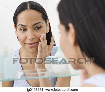 Stock Image - African woman applying face cream in mirror. Fotosearch