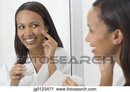 Stock Photo - African woman applying face cream in mirror. Fotosearch