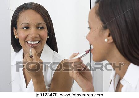 Stock Photo - African woman applying lipstick in mirror . Fotosearch