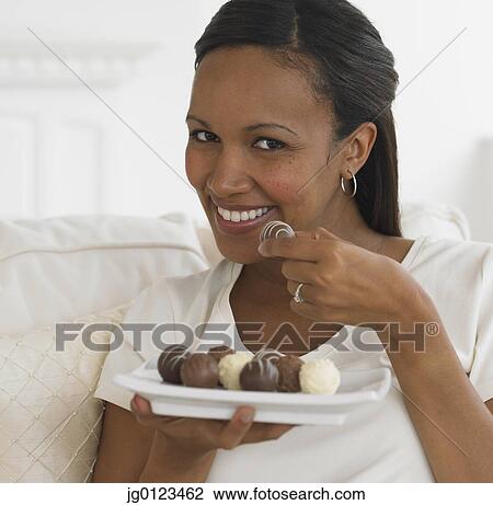 Stock Image - African woman eating chocolate truffles. Fotosearch