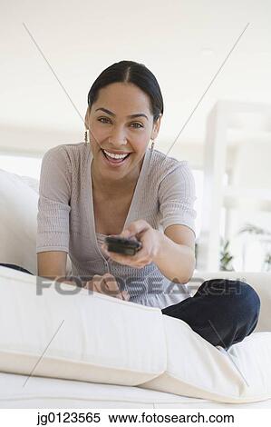 Stock Photography - African woman on sofa pointing remote control. Fotosearch