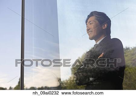 Stock Image - Asian businessman looking through window. Fotosearch