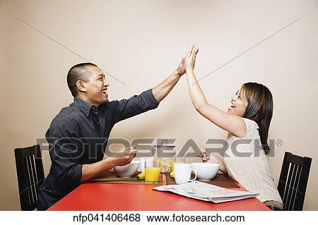 Asian couple high-fiving at breakfast table View Large Photo Image Stock Photo - Asian couple high-fiving at breakfast table. Fotosearch