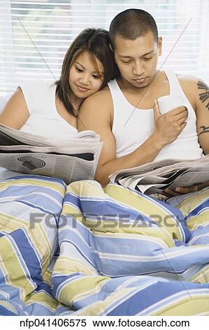 Stock Photography - Asian couple reading newspaper in bed. Fotosearch