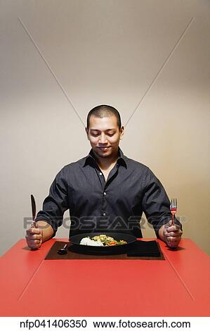 Stock Image - Asian man at table with full plate of food. Fotosearch