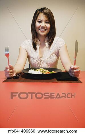 Stock Image - Asian woman at table with full plate of food. Fotosearch