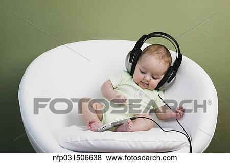 Stock Photo - Baby in chair wearing adult headphones. Fotosearch