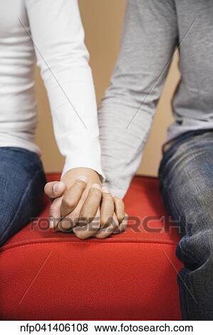 Couple holding hands on sofa View Large Photo Image Stock Photo - Couple holding hands on sofa. Fotosearch