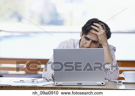 Stock Image - Hispanic businessman looking at laptop with hand on forehead. Fotosearch