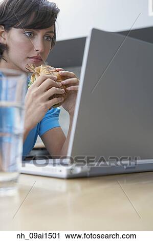 Hispanic woman looking at laptop and eating View Large Photo Image Stock Image - Hispanic woman looking at laptop and eating. Fotosearch