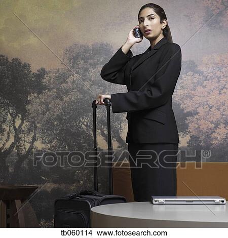 Indian businesswoman holding suitcase and talking on cell phone View Large Photo Image Picture - Indian businesswoman holding suitcase and talking on cell phone. Fotosearch