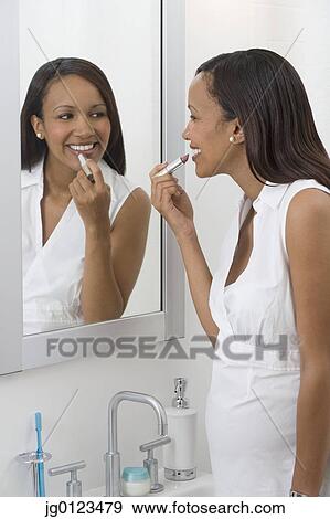 Stock Photo - Pregnant African woman applying lipstick in mirror. Fotosearch