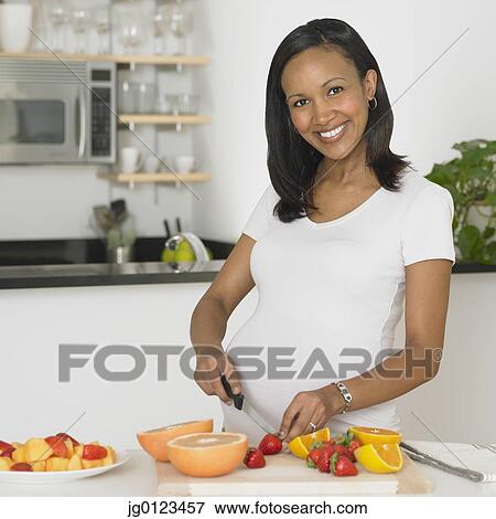 Stock Photo - Pregnant African woman chopping fruit. Fotosearch