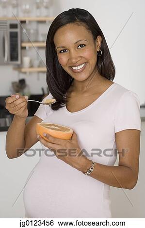 Stock Photograph - Pregnant African woman eating grapefruit. Fotosearch