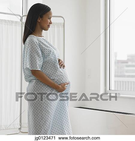 Stock Image - Pregnant African woman in hospital looking out window. Fotosearch
