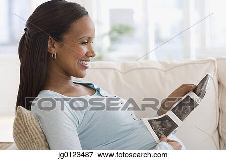 Stock Photo - Pregnant African woman looking at ultrasound printout. Fotosearch