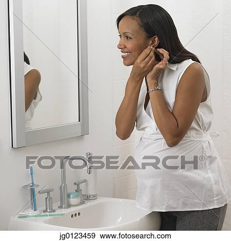 Pregnant African woman putting on earring in bathroom View Large Photo Image Stock Photo - Pregnant African woman putting on earring in bathroom. Fotosearch