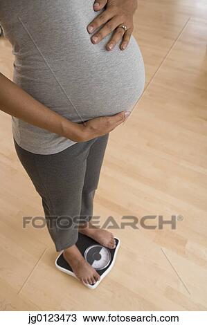 Stock Image - Pregnant African woman standing on scale. Fotosearch