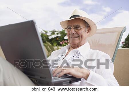Senior man typing on laptop in lounge chair View Large Photo Image Stock Image - Senior man typing on laptop in lounge chair. Fotosearch
