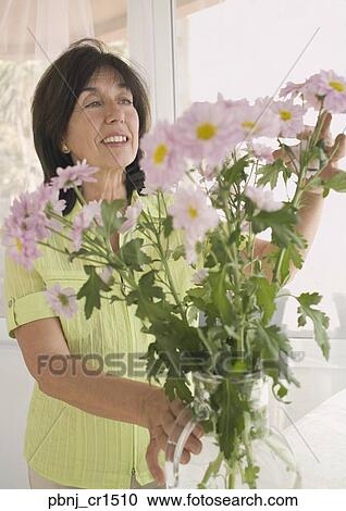 Stock Image - Senior woman arranging flowers in vase. Fotosearch
