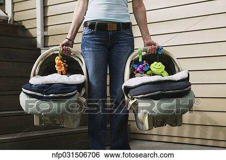 Stock Photograph - Woman carrying two baby car seats. Fotosearch