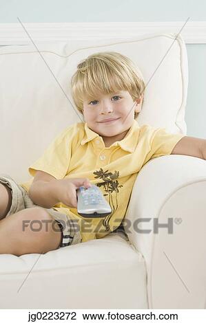 Stock Image - Young boy on sofa pointing remote control. Fotosearch