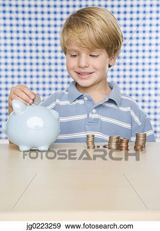 Stock Photo - Young boy putting change in piggy bank. Fotosearch