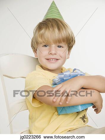 Stock Photograph - Young boy wearing party hat and holding gift. Fotosearch