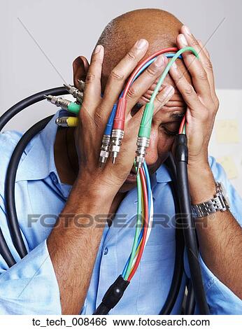 Stock Photograph - African businessman holding computer cables with head in hands. Fotosearch