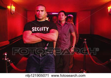Stock Image - African male bouncer with arms crossed in front of people. Fotosearch